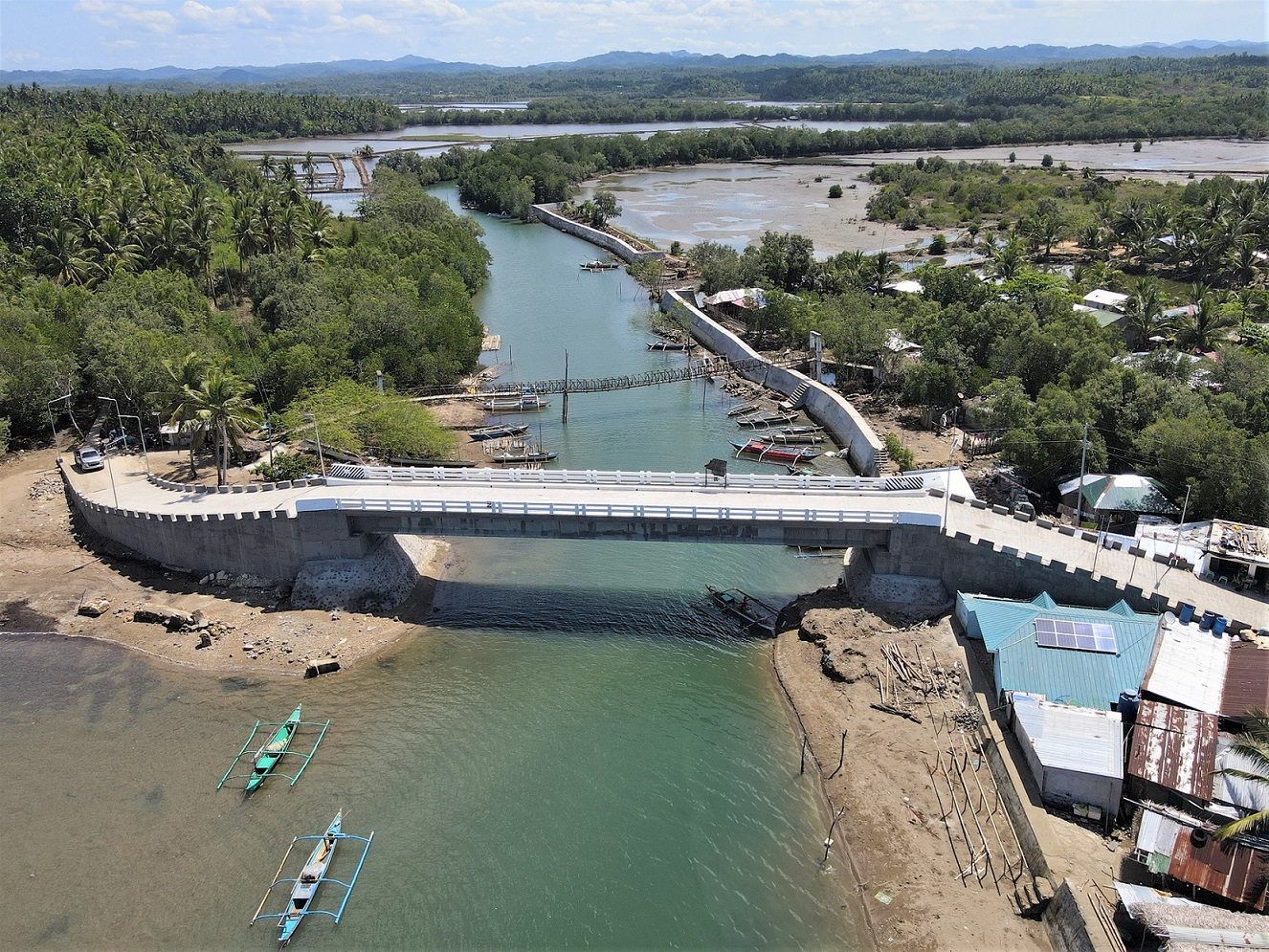 A newly constructed bridge and flood control system over a river, surrounded by lush greenery and coastal homes.