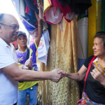 Allan Reyes warmly shaking hands with a female resident during a community visit.